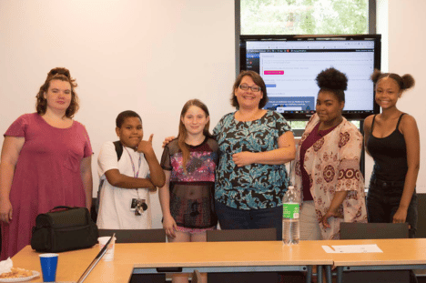 Copyright 2024 Digital Bridges International. All rights reserved. Founder Connie Capiotis with young workshop participants standing and smiling in the classroom.