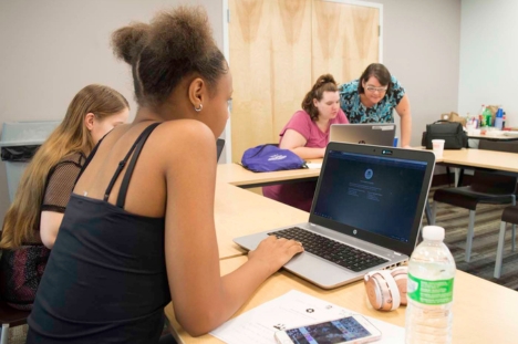 Copyright 2024 Digital Bridges International. All rights reserved. Founder Connie Capiotis. Woman working on laptop in a classroom setting.