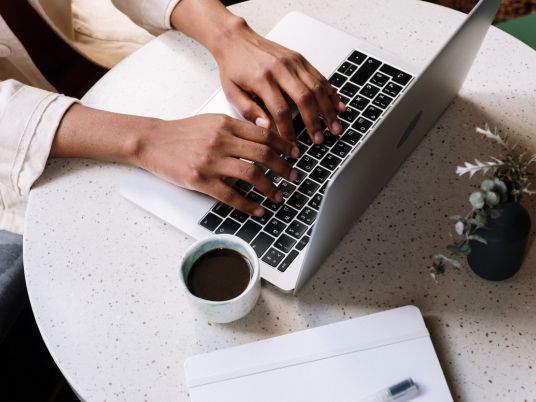 Copyright 2024 Digital Bridges International. All rights reserved. Founder Connie Capiotis. Person working on laptop with coffee cup.