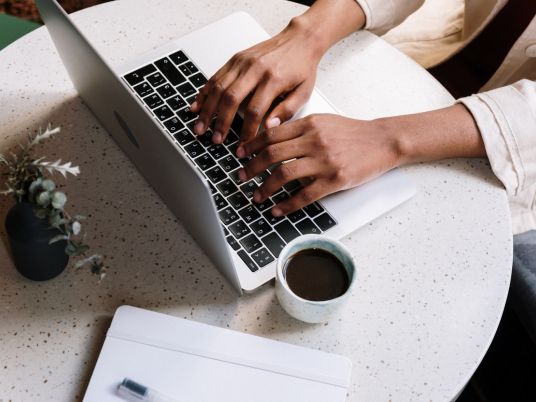 Copyright 2024 Digital Bridges International. All rights reserved. Founder Connie Capiotis Person working on laptop with coffee cup nearby